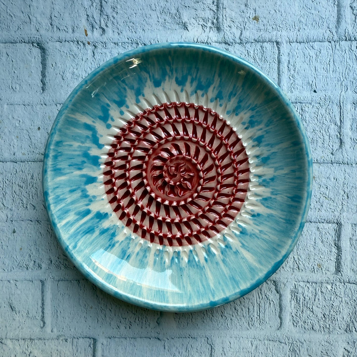 Ceramic plate with blue and red design on a textured gray surface