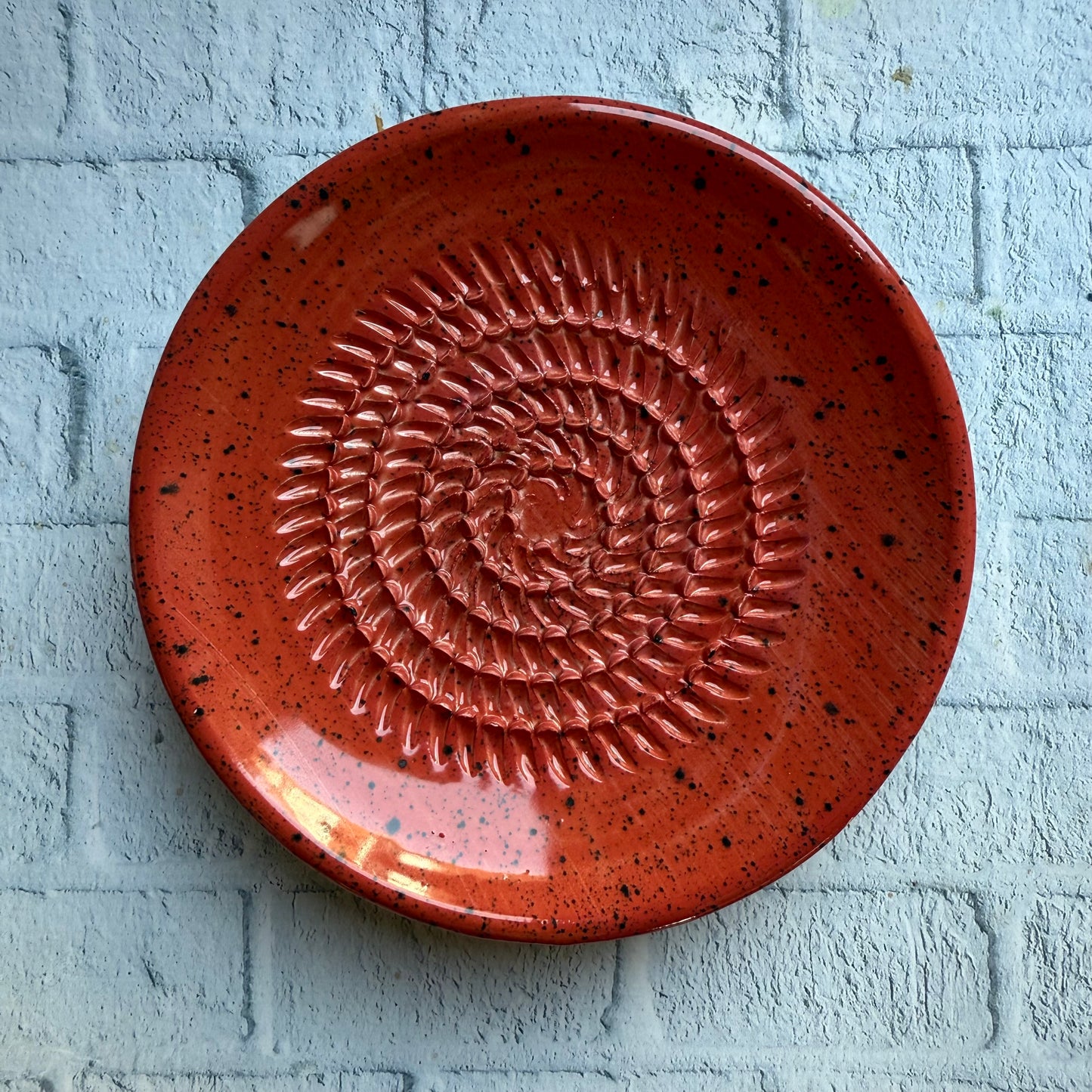 Red ceramic plate with a textured design on a light blue brick wall.